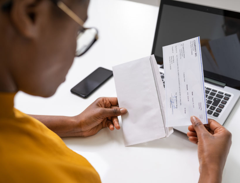 Woman in yellow top reviewing her paycheck and pay stub with laptop in background